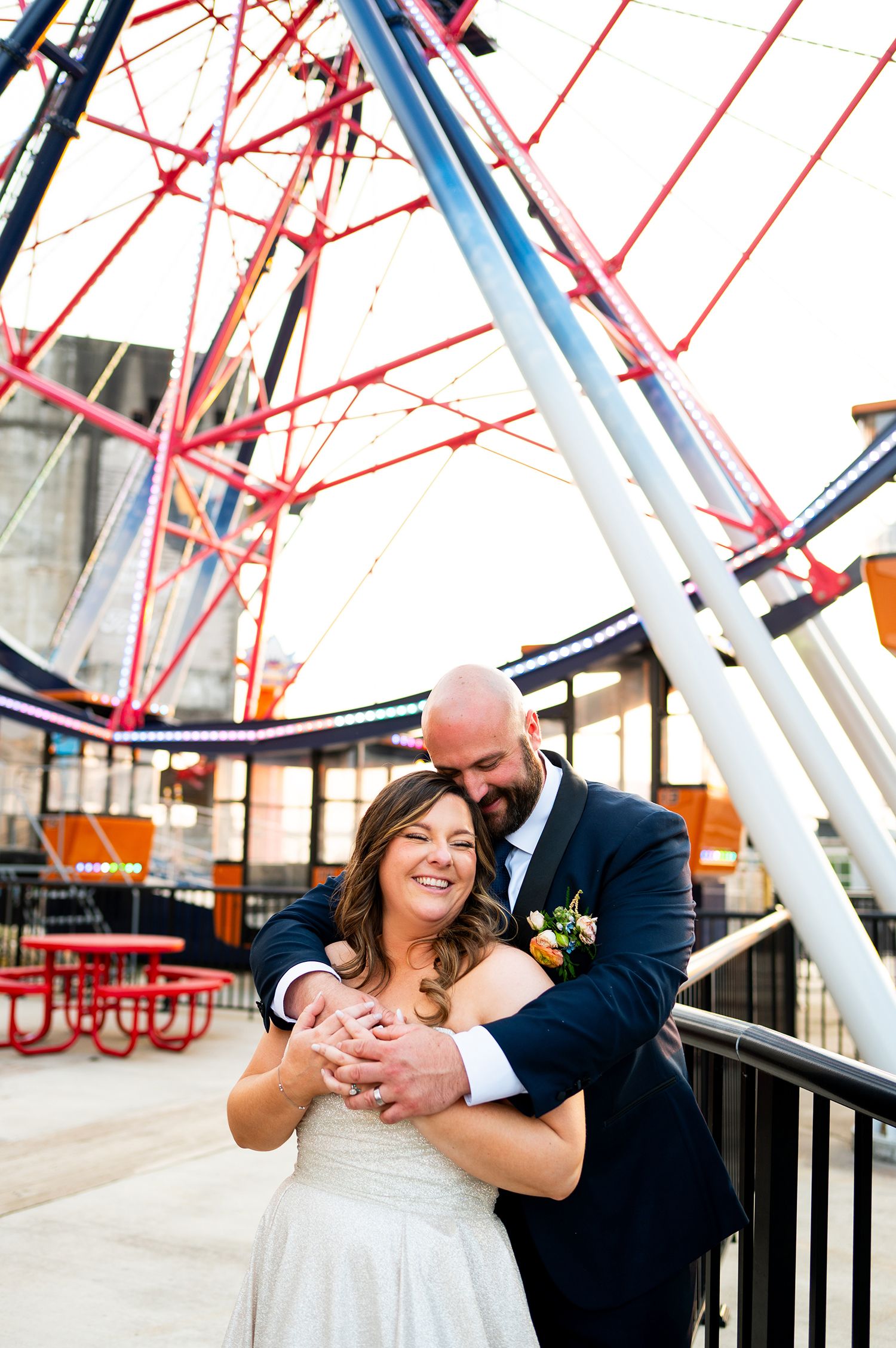 A couple shares a romantic moment near a large red and white carnival ride structure.