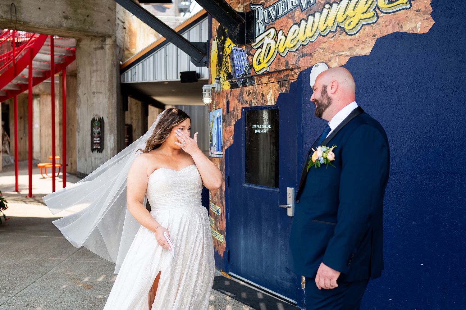 A couple shares a candid moment outside a building with vintage signage on their wedding day.