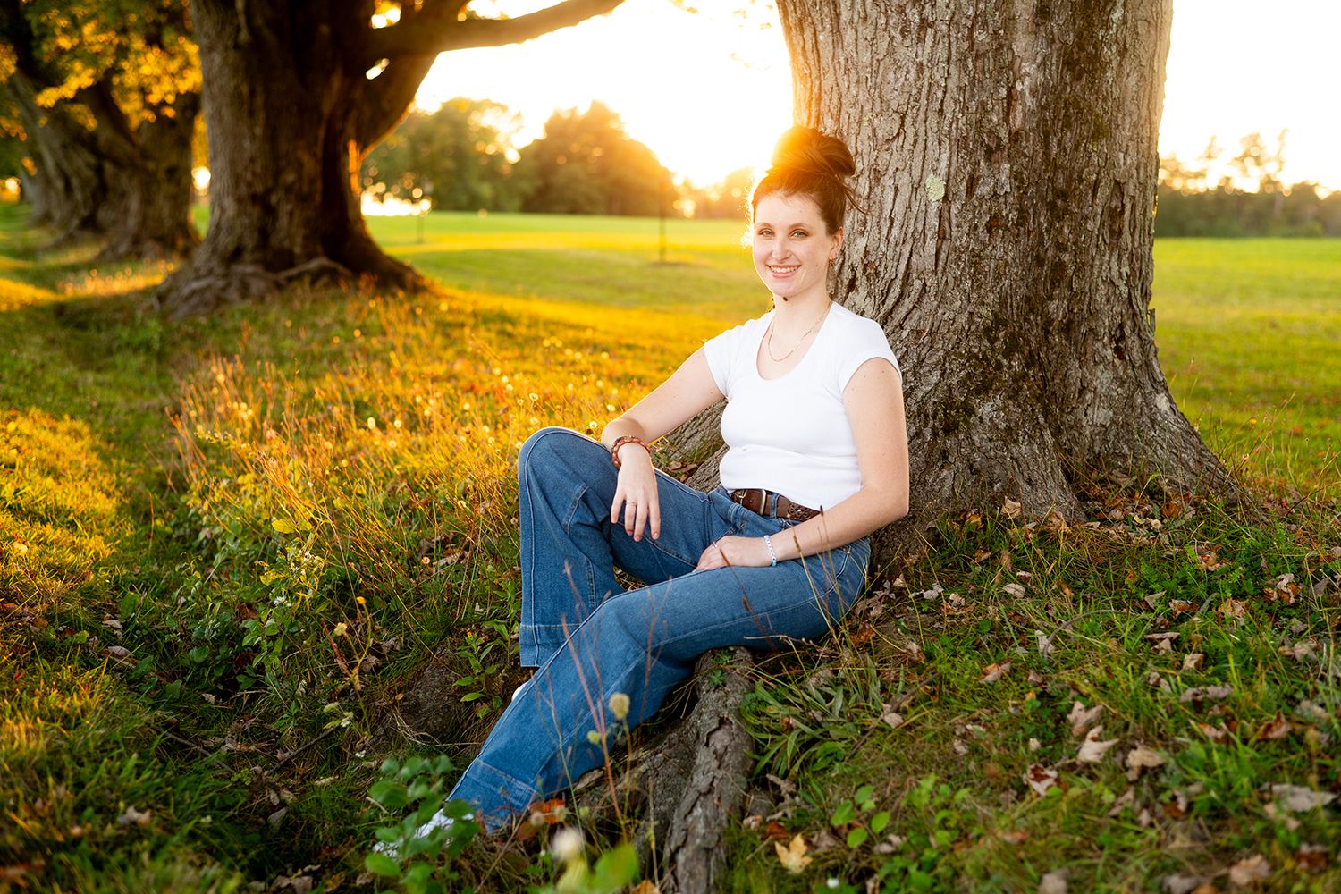 Outdoor portrait series at sunset showing someone resting against a tree trunk in a natural parklike setting.