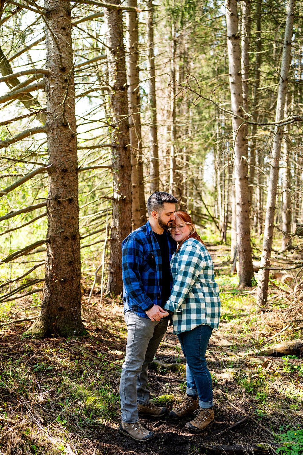 Among tall pine trees in a wooded forest, a couple embraces while enjoying a romantic nature walk.