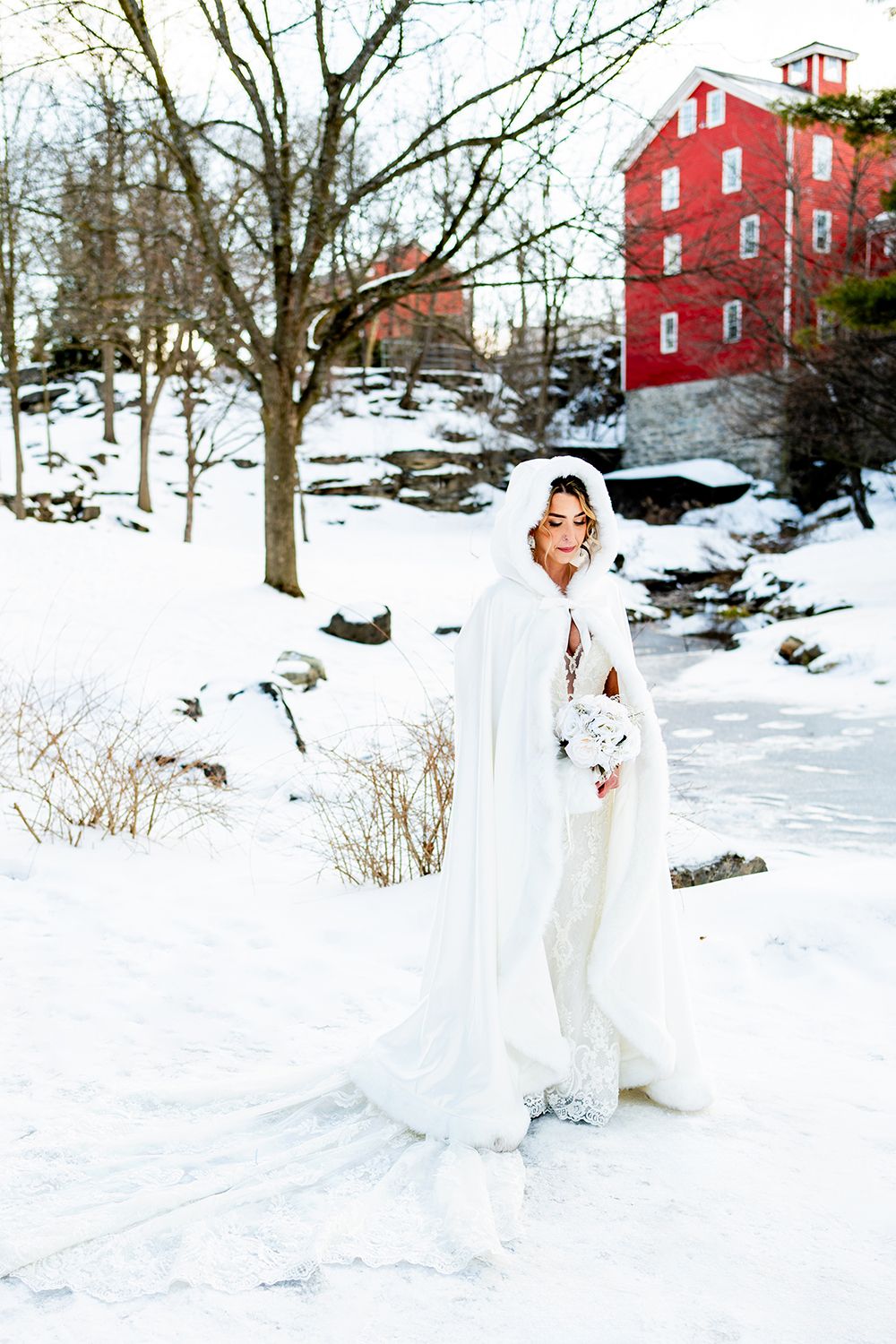 A snowy winter scene with a bright red barn in the background and a beautiful white gown stands out against the pristine landscape.