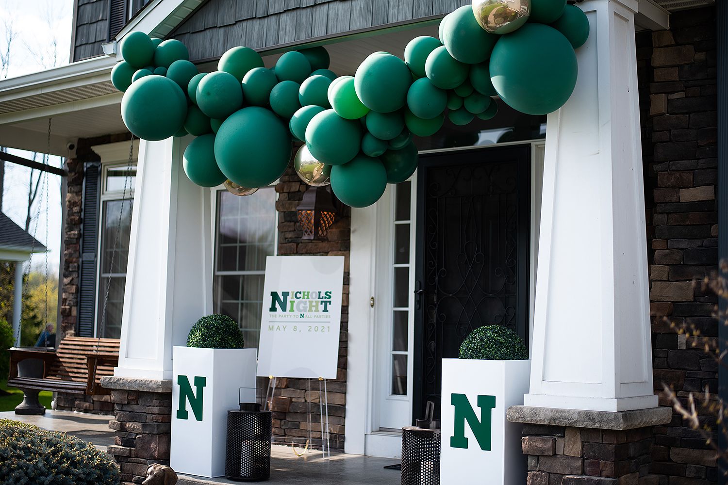 Green balloon arch and decorative columns adorn a building entrance displaying the letter N for a celebration.