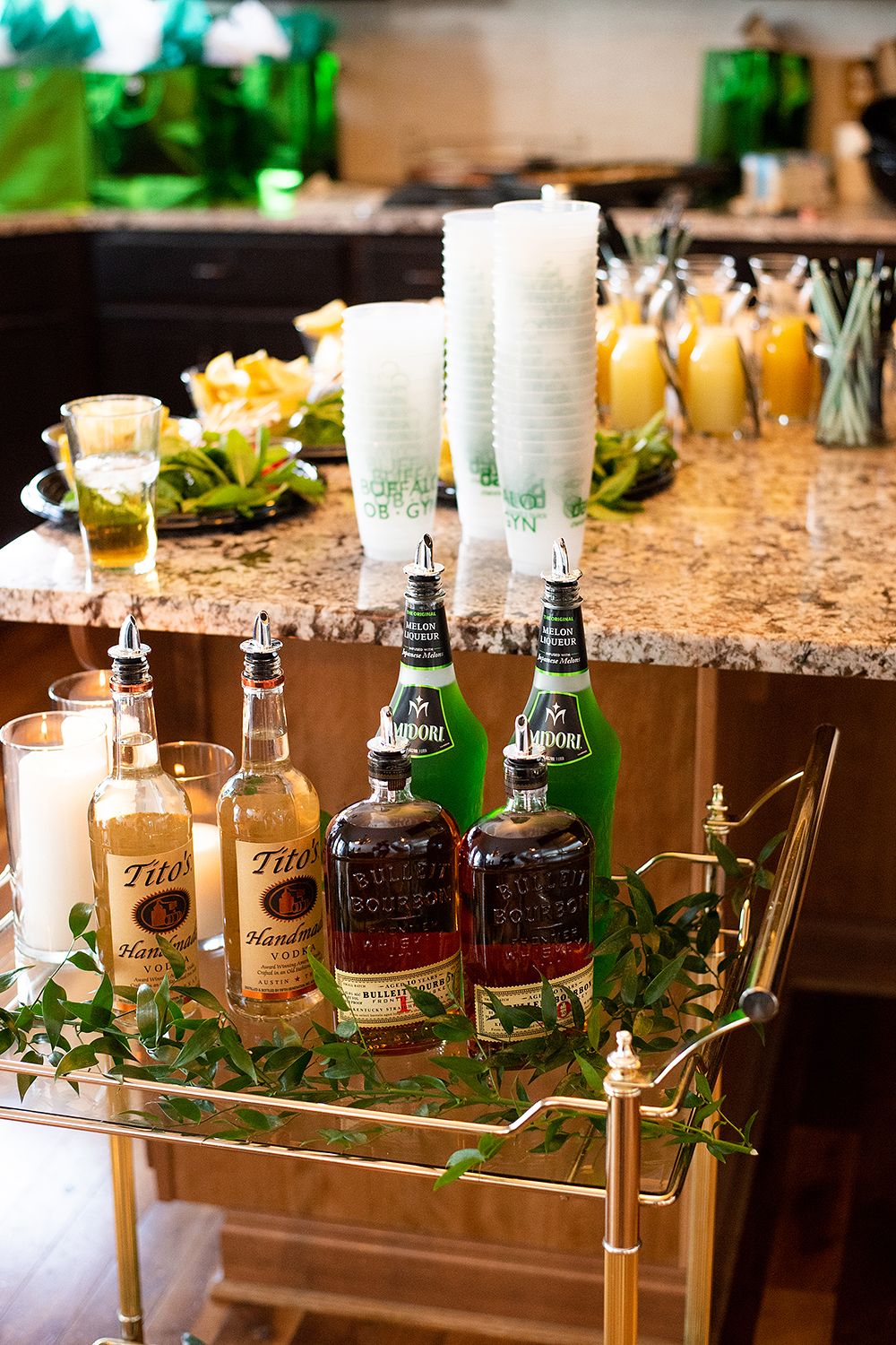 A bar cart with Tito's vodka bottles and mixers displayed on a gold-trimmed serving cart next to a marble countertop.