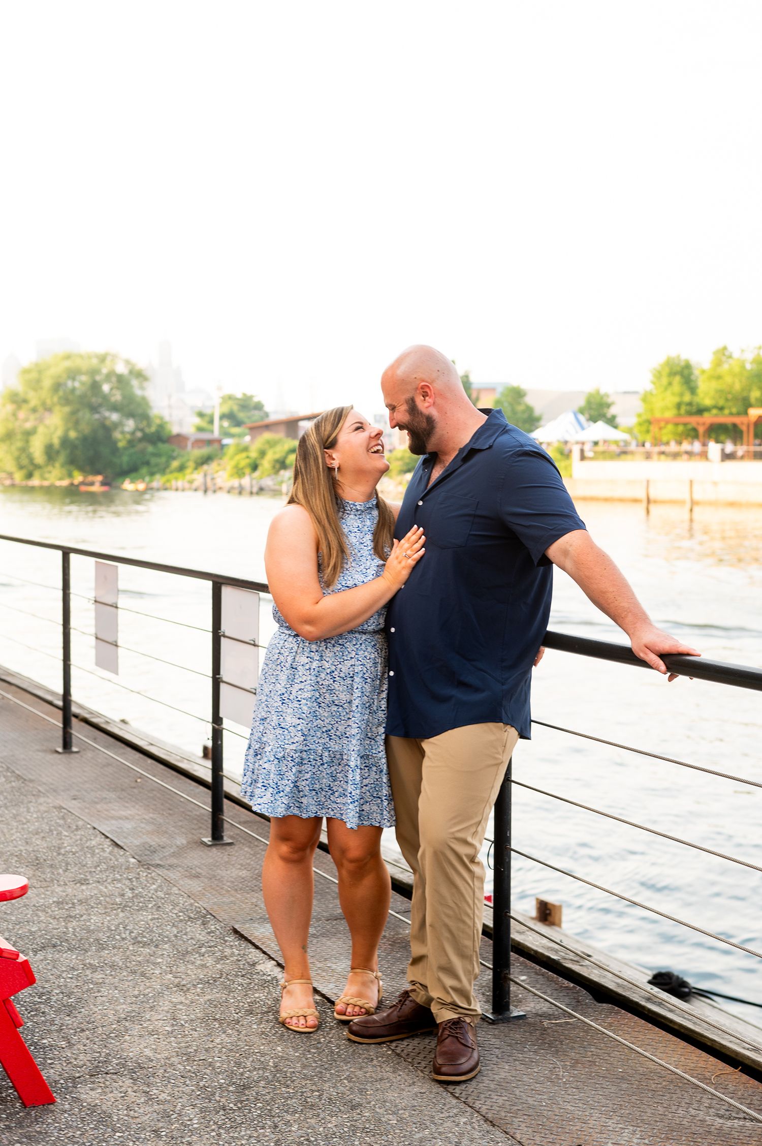 Couple laughing together on a waterfront boardwalk, woman in blue dress and man in navy shirt.