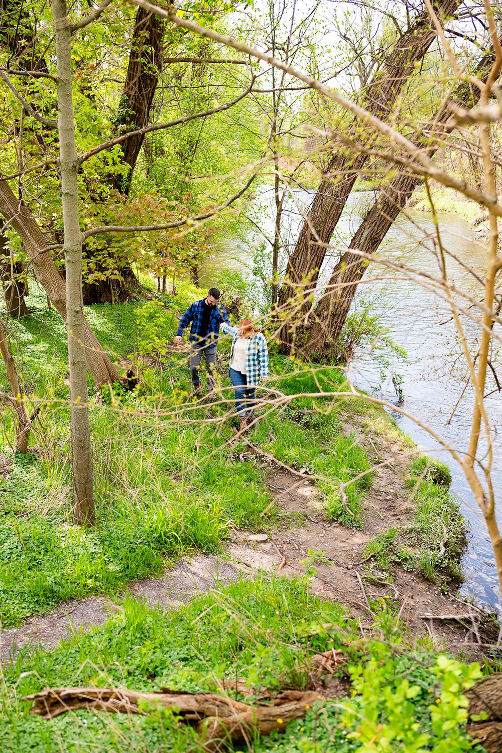 People exploring a scenic wooded trail along a peaceful riverside on a spring afternoon.