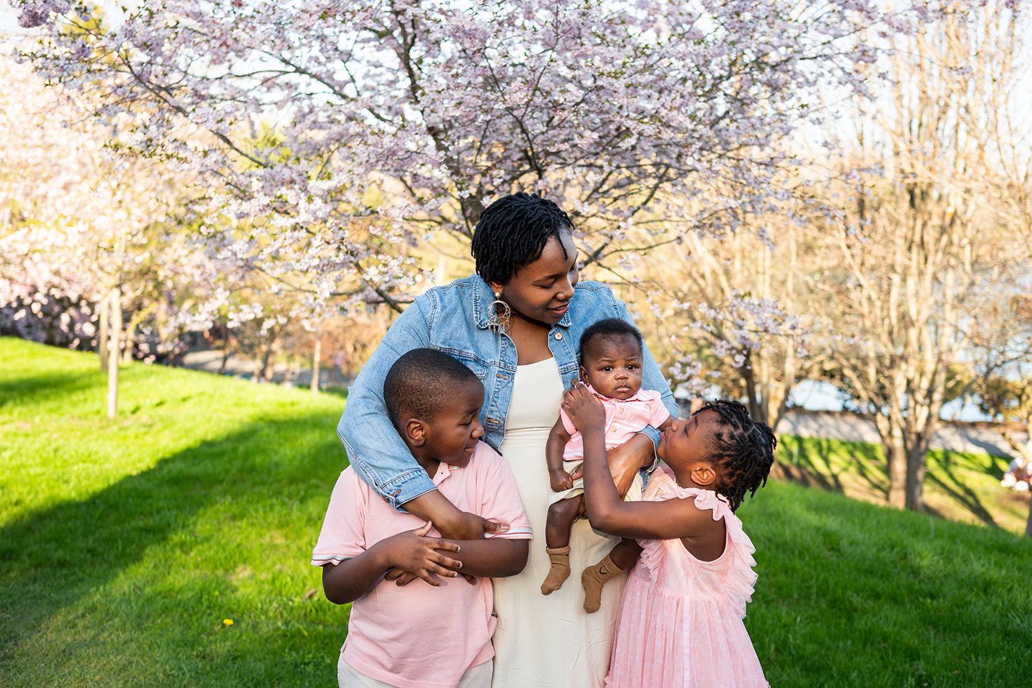 A family enjoying a spring day together under blooming cherry blossom trees in a lush green park.