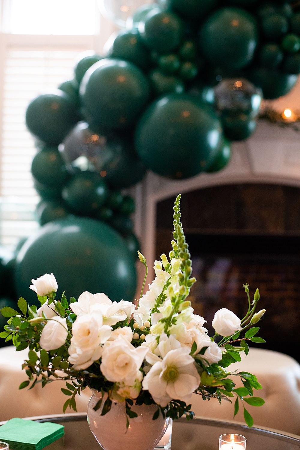 Elegant floral centerpiece with white flowers and green balloon arch decoration in an indoor party setting.