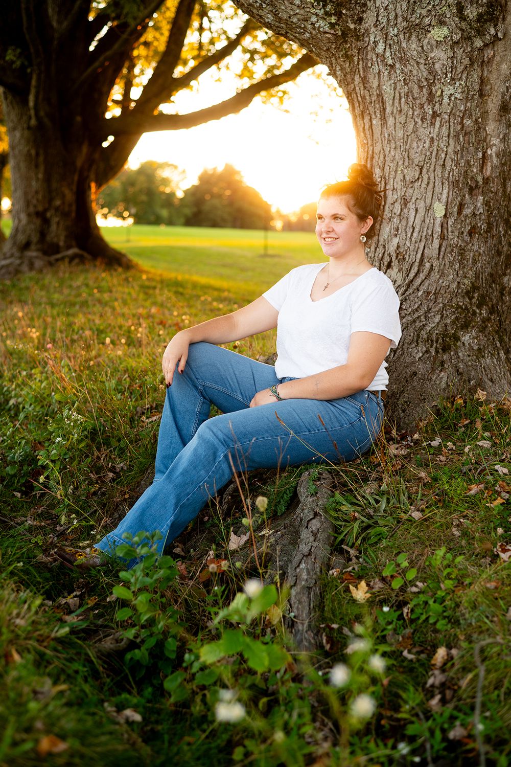 Portrait photo of someone sitting against a large tree trunk at sunset with golden light filtering through the branches.