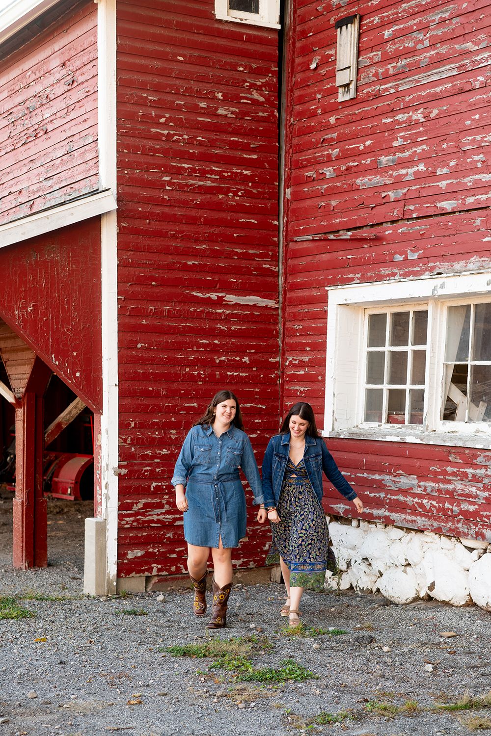 Two people walk together in casual clothing against a weathered red barn with peeling paint and white trim.