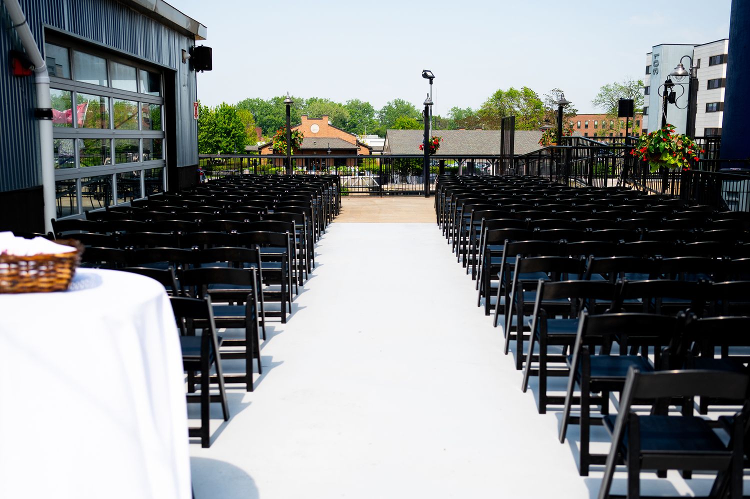 Wedding ceremony setup with rows of black chairs and white decorations outdoors.