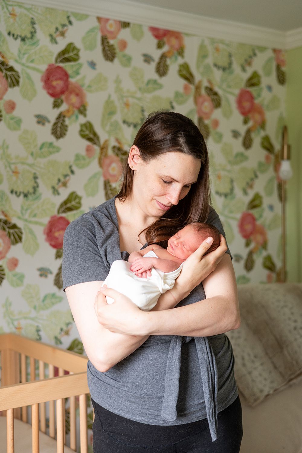 A peaceful moment between caregiver and newborn in a nursery with floral wallpaper.