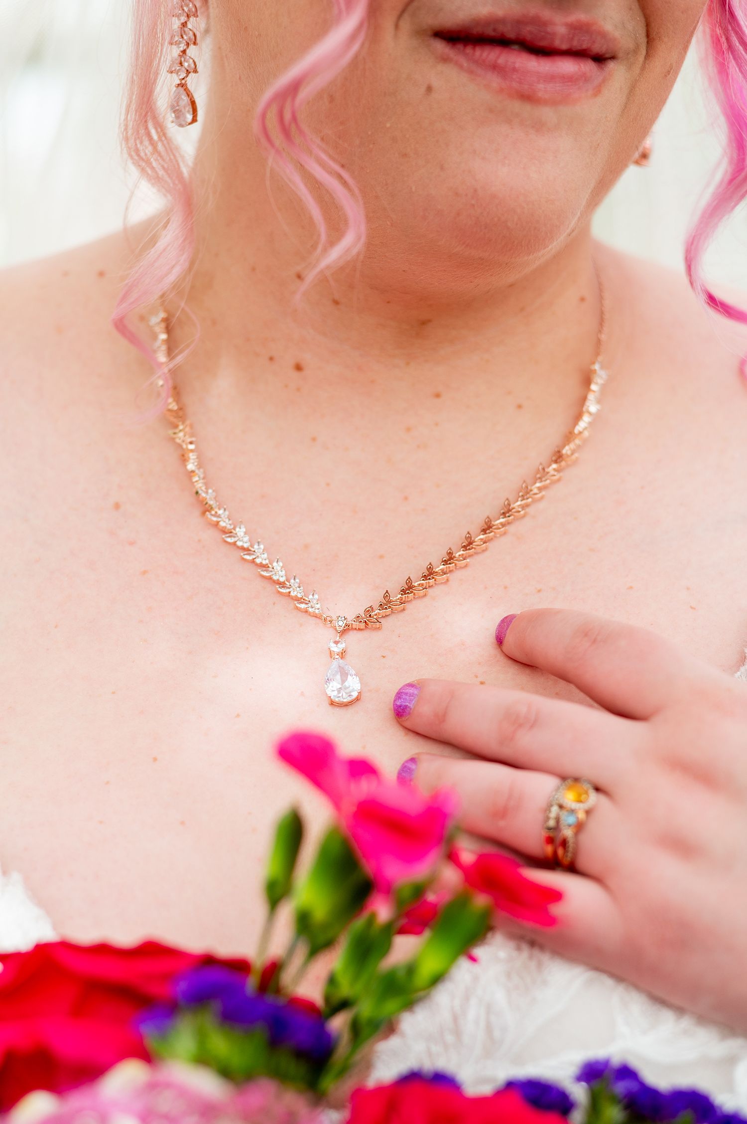 Close-up of bride with pink hair wearing a rose gold diamond necklace and ring, holding a vibrant pink and purple bouquet.