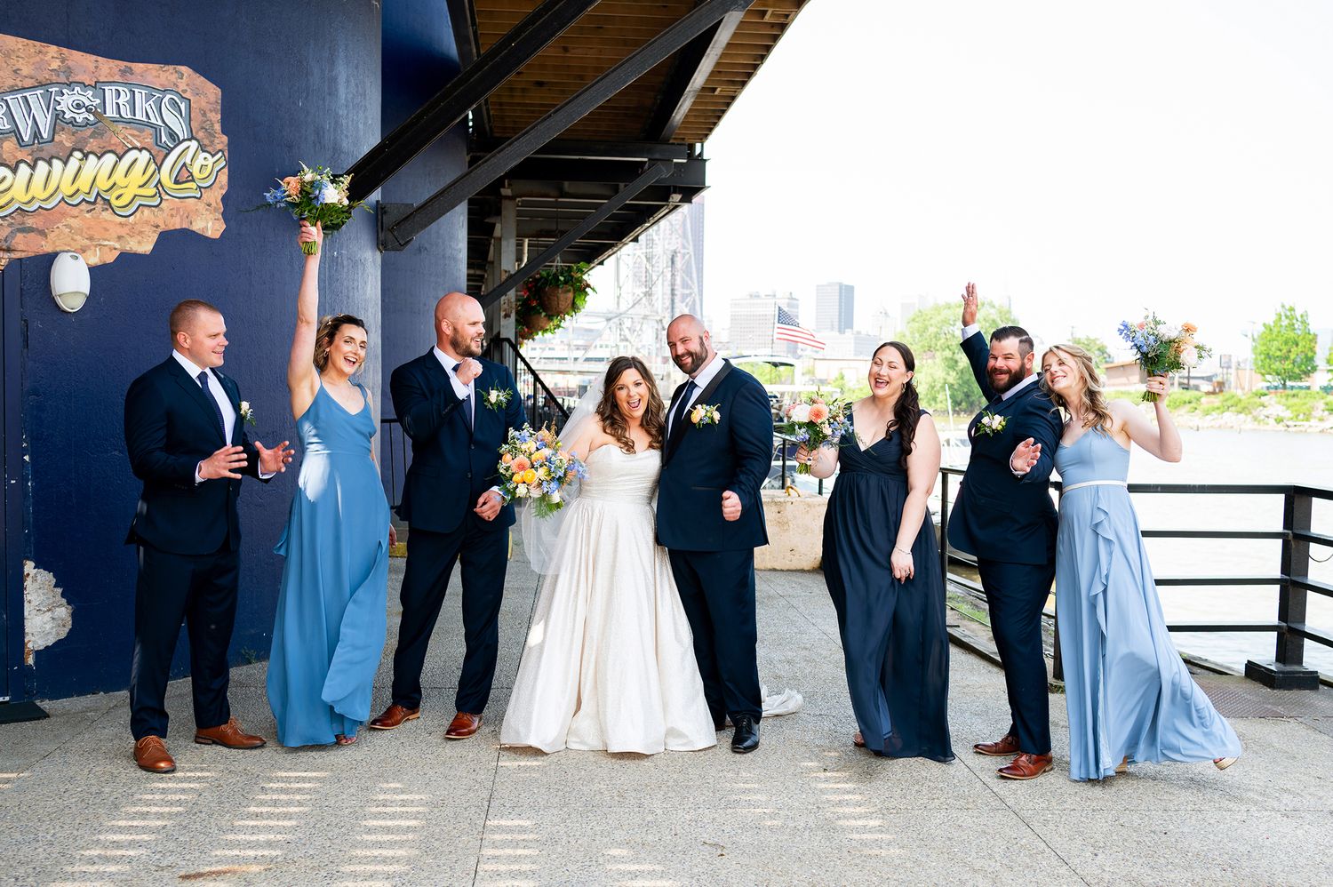 Wedding party poses together on a deck with industrial backdrop wearing navy and light blue attire.