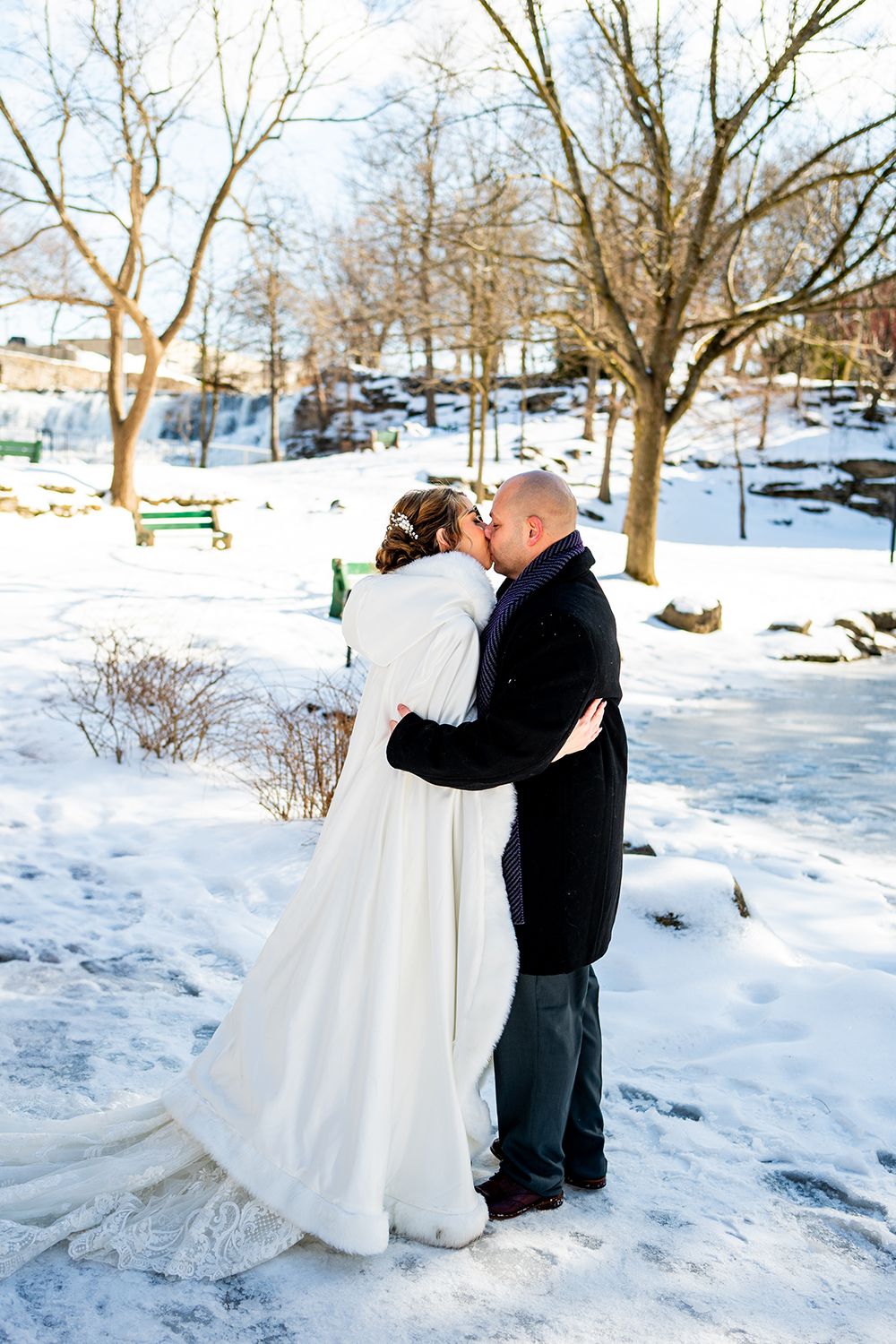 Newlyweds share an intimate kiss during their winter wedding photoshoot in a snow-covered park.