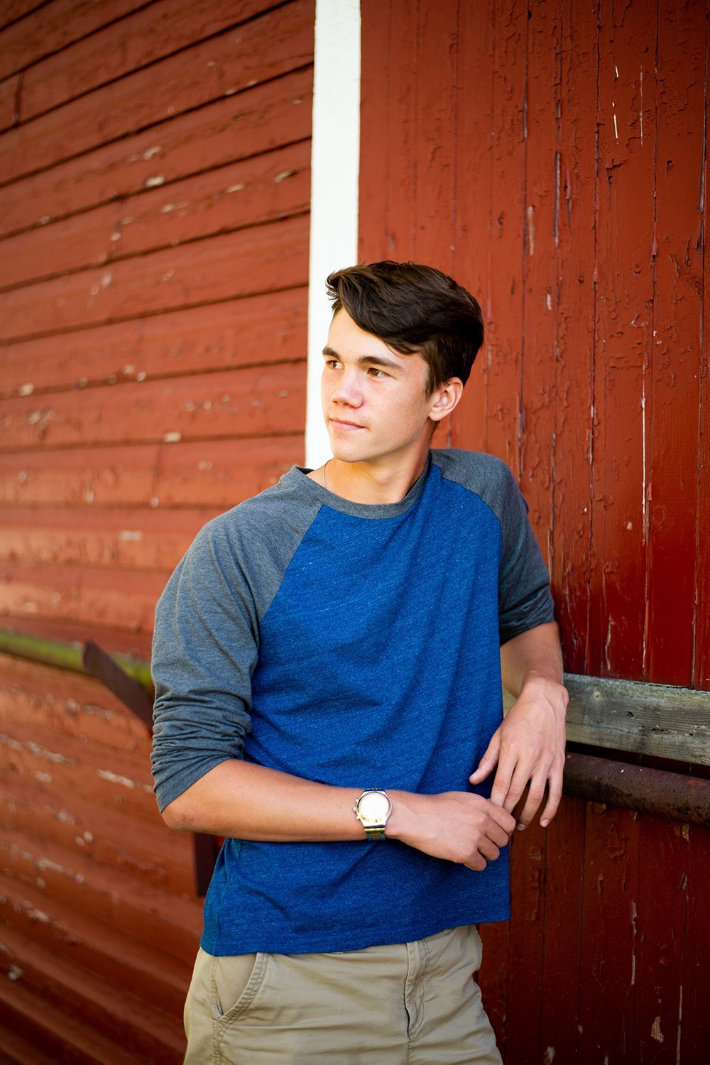 Portrait of a person wearing a blue and gray raglan shirt leaning against a red barn wall.