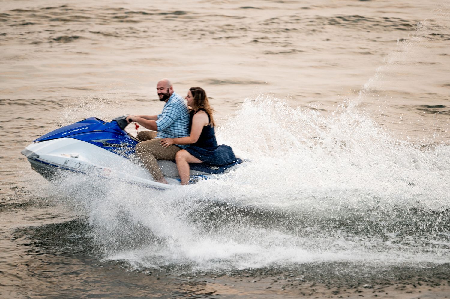 Two people riding a blue and white jet ski on choppy water, creating large splashing waves.