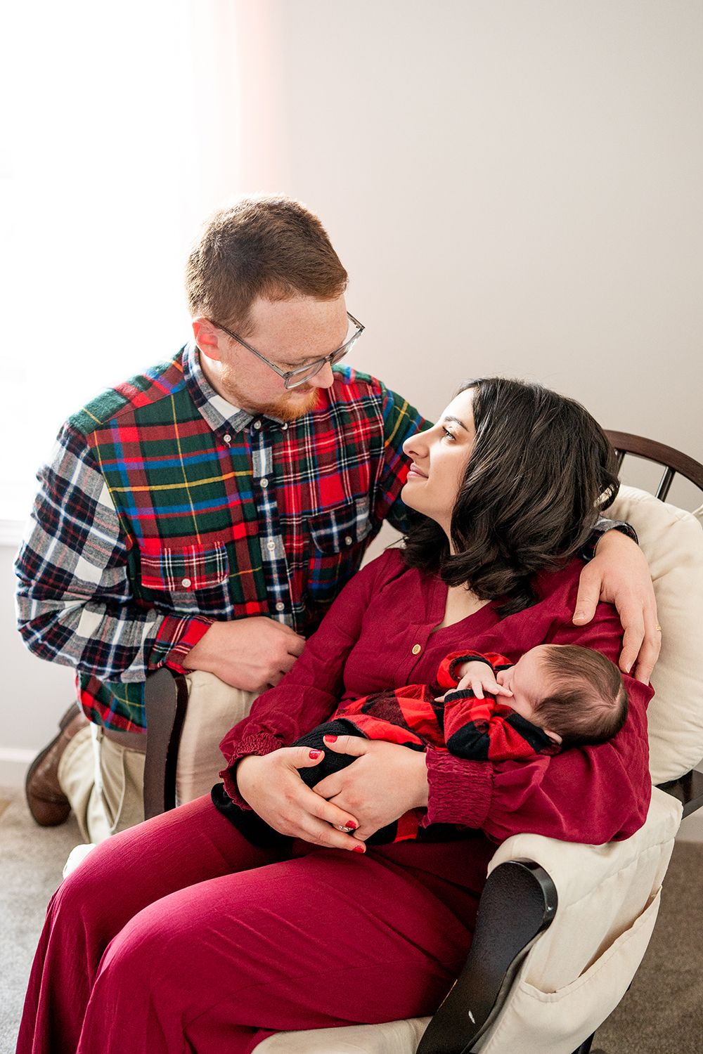 A couple in matching holiday plaid and burgundy outfits share sweet moments together on a light-colored couch.