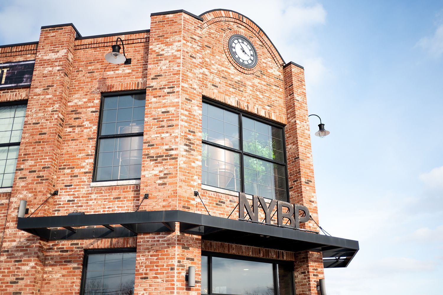 Historic brick building exterior with clock feature and decorative black metal awning against blue sky.
