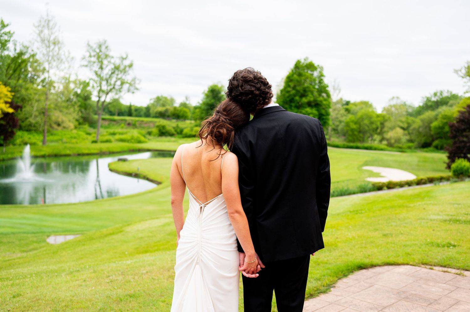 A couple walks along a scenic golf course path surrounded by lush green grass and water features on a sunny day.
