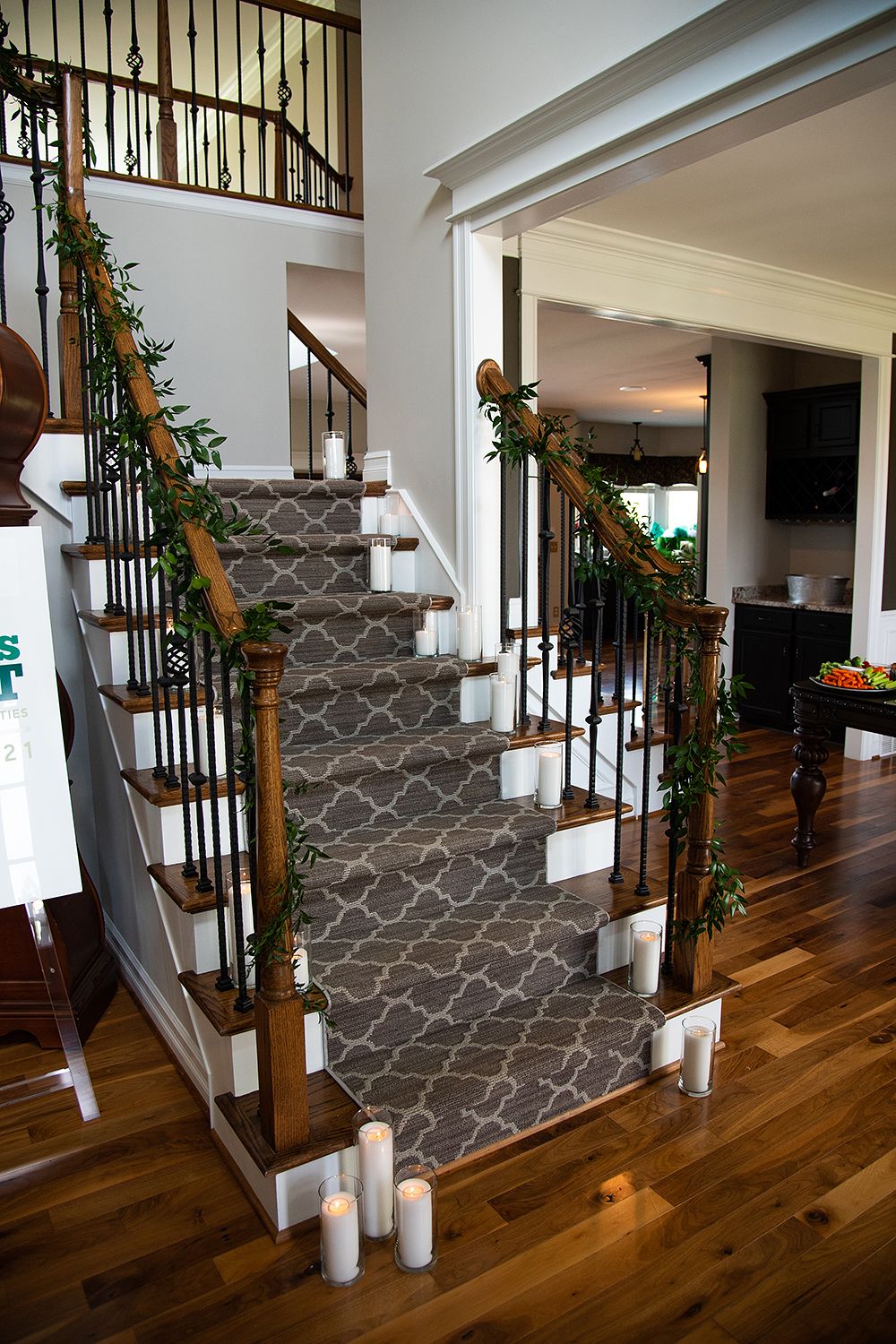 A staircase decorated with garland for the holidays features dark hardwood floors and modern gray patterned wallpaper.