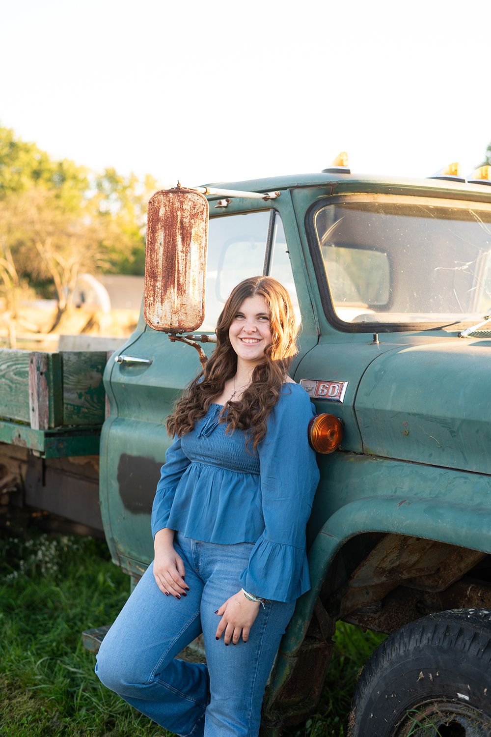 A rustic outdoor photoshoot featuring a person in blue against an old turquoise pickup truck during golden hour.