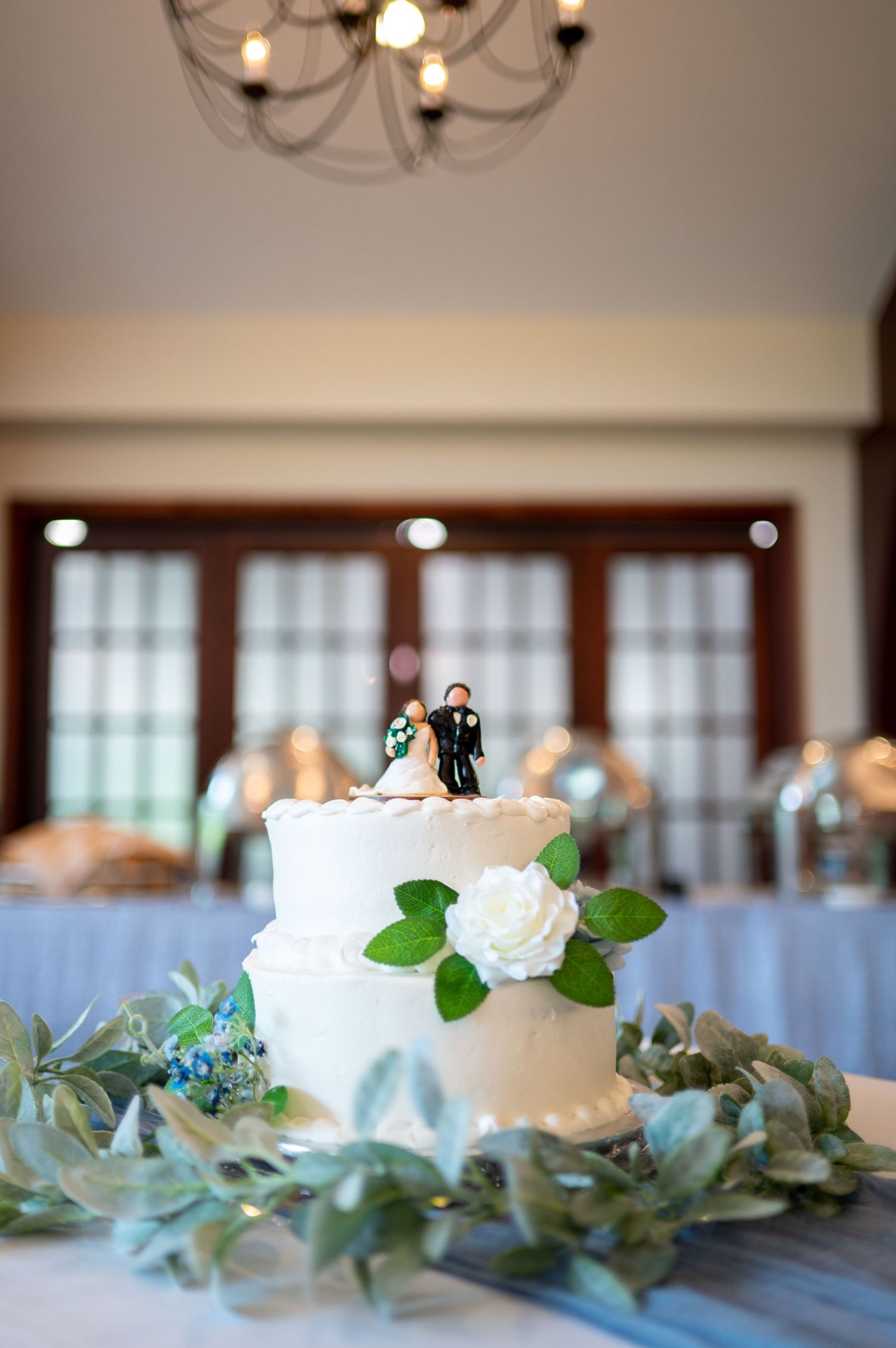 Elegant wedding cake topper and eucalyptus garland decorations on display at an indoor reception venue.