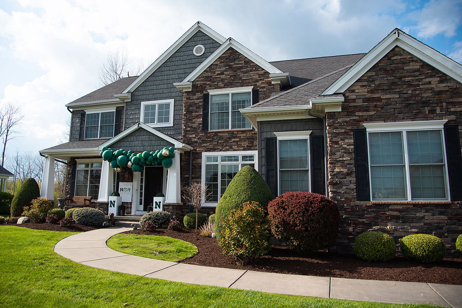Luxury stone and vinyl siding house with well-maintained landscaping and curved walkway leading to covered front entrance.