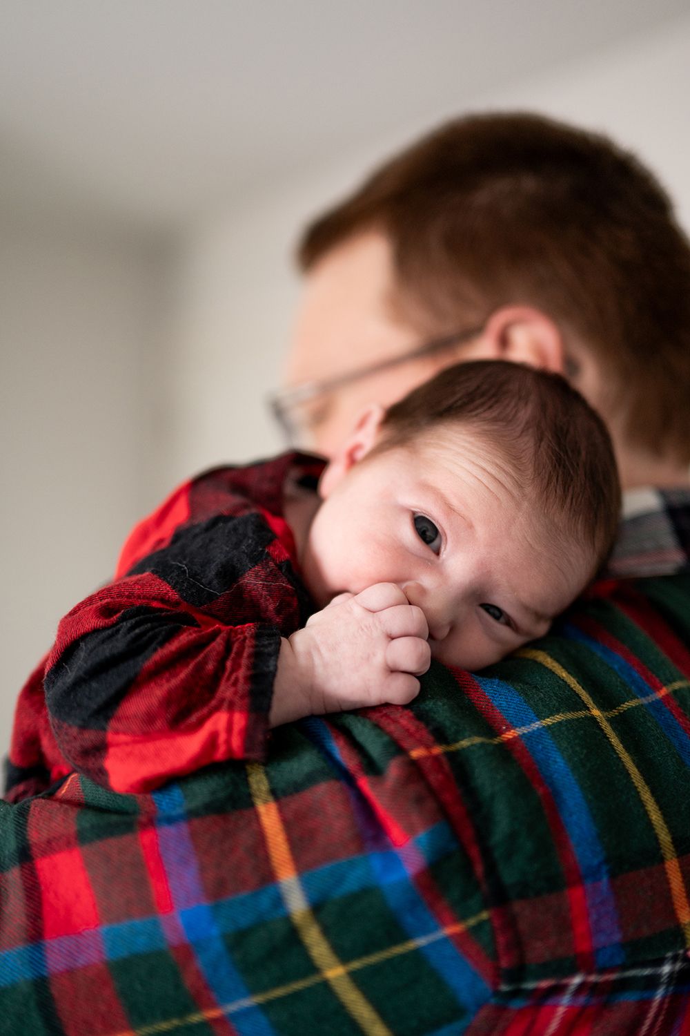 A small child in a red plaid shirt rests their head on someone's shoulder.