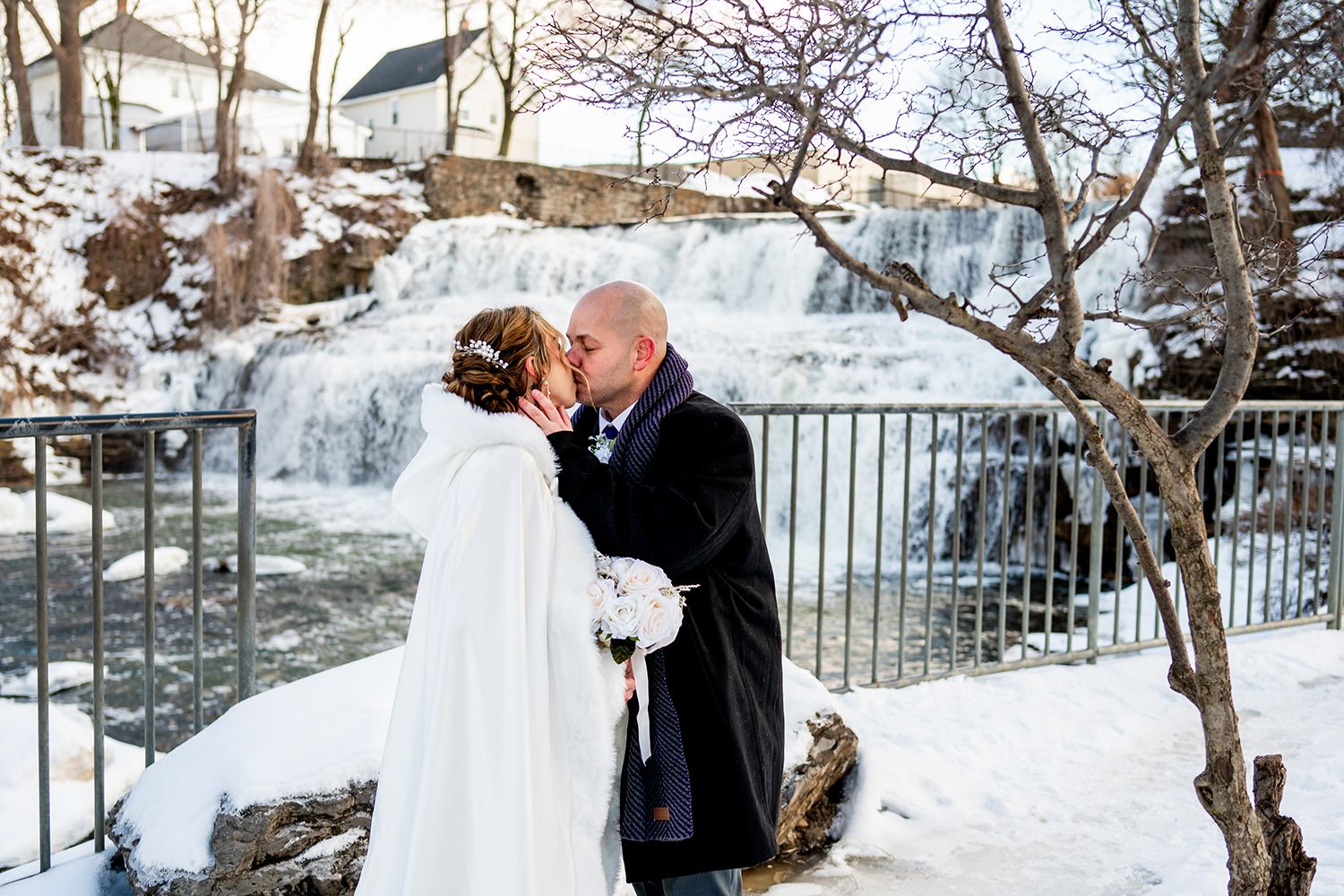 A romantic winter wedding moment captured near a frozen waterfall with snow-covered trees.