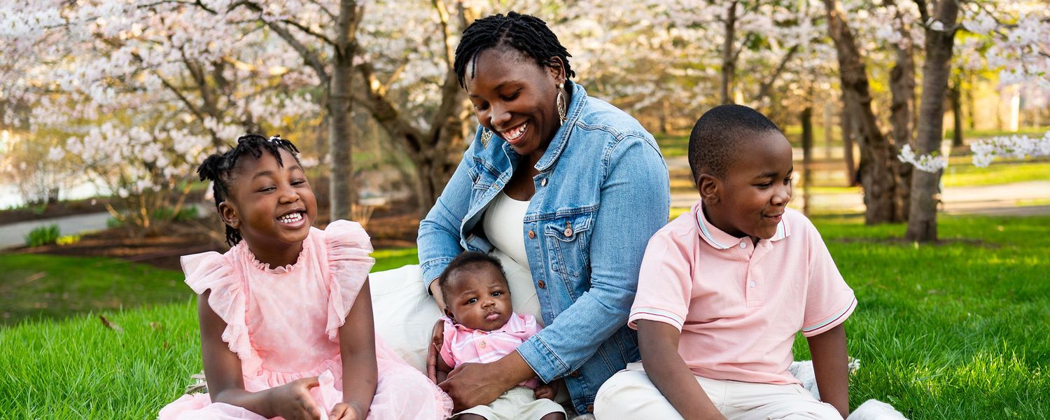 An outdoor family gathering shows two adults and children playing on a grassy lawn in springtime.