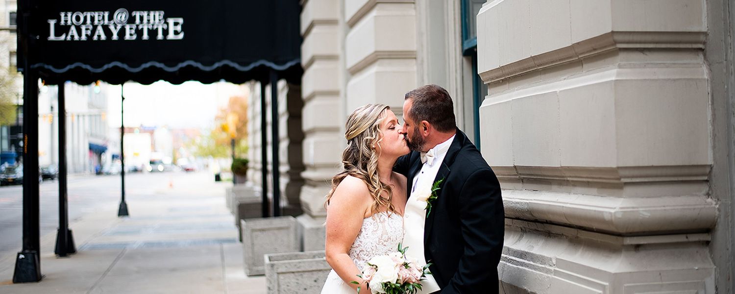 Wedding party poses outside ornate stone building entrance for elegant formal photographs.
