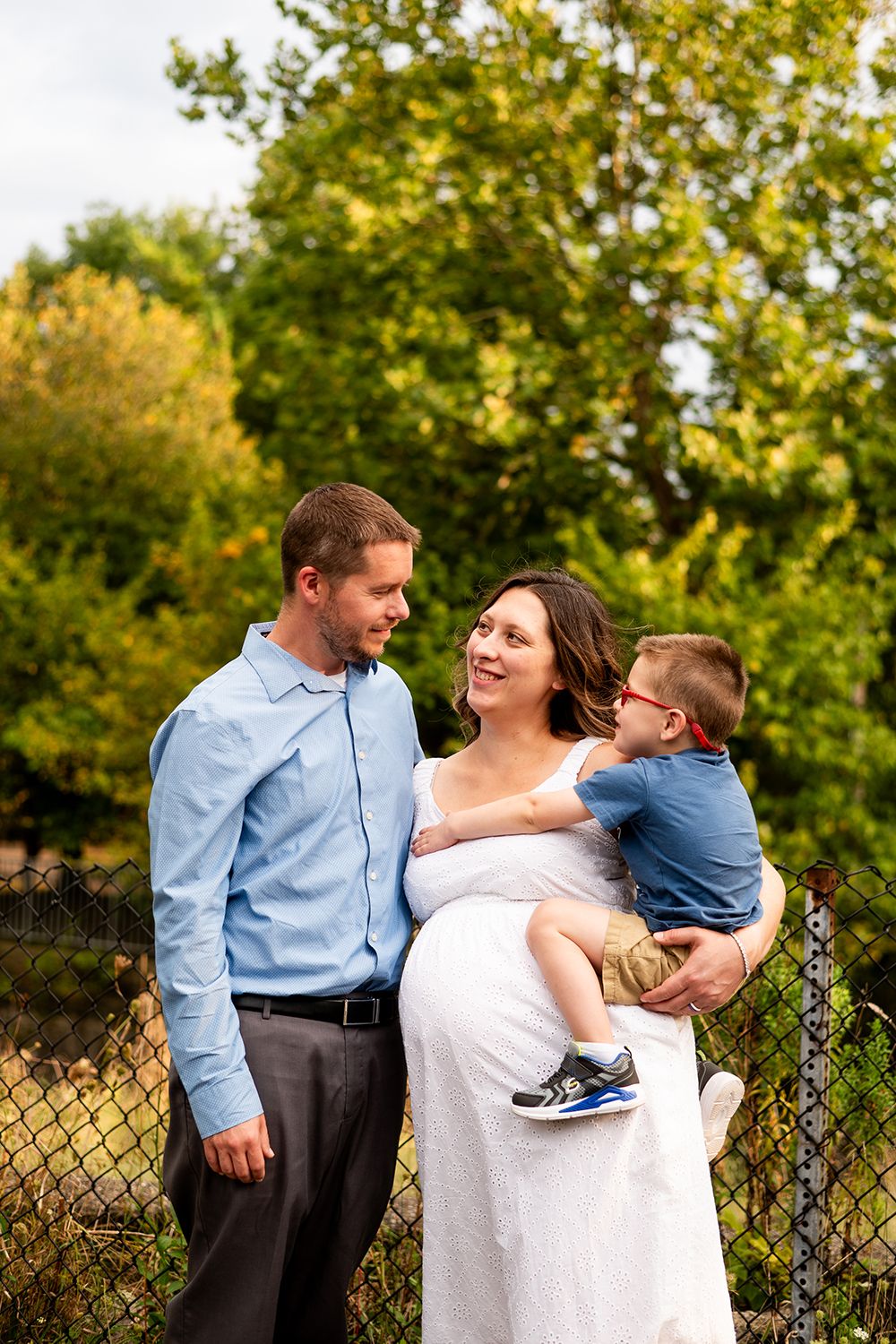 A family shares a joyful moment together outdoors against a backdrop of lush green trees and a chain-link fence.