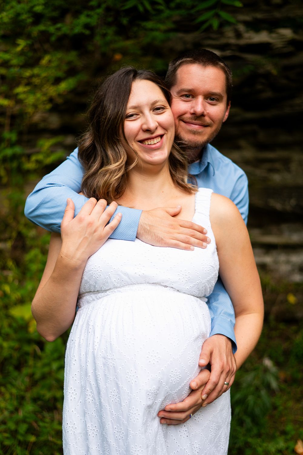 A couple in white dress and blue shirt share intimate moments against a natural outdoor backdrop with rock formations.