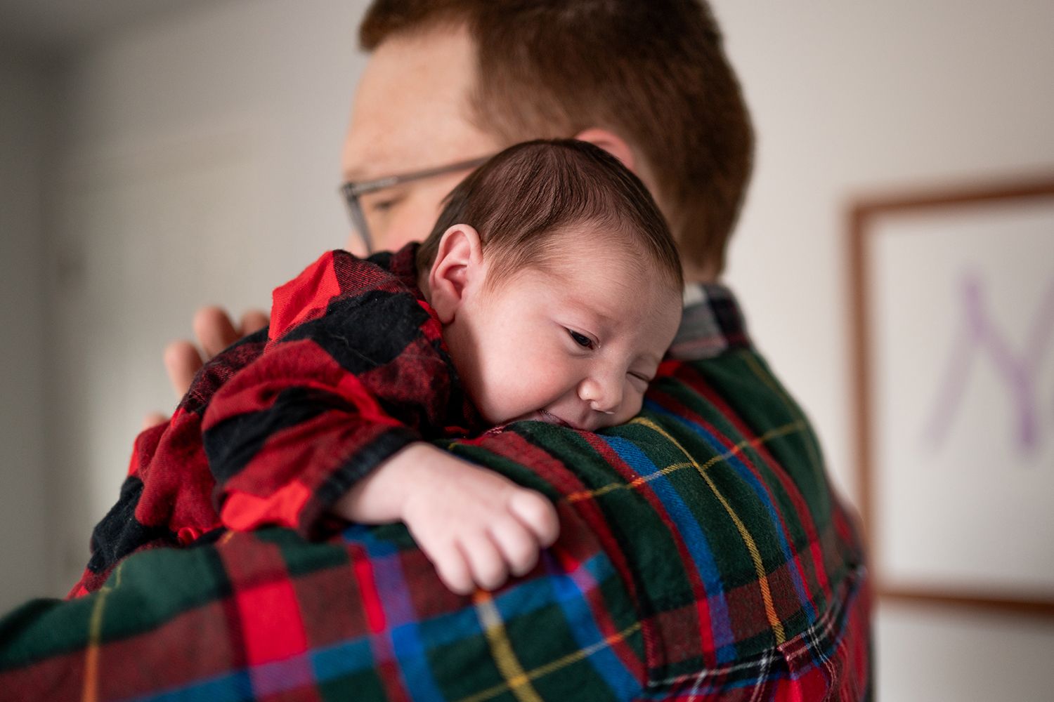 A small child rests peacefully against someone wearing a red and black buffalo plaid flannel shirt.