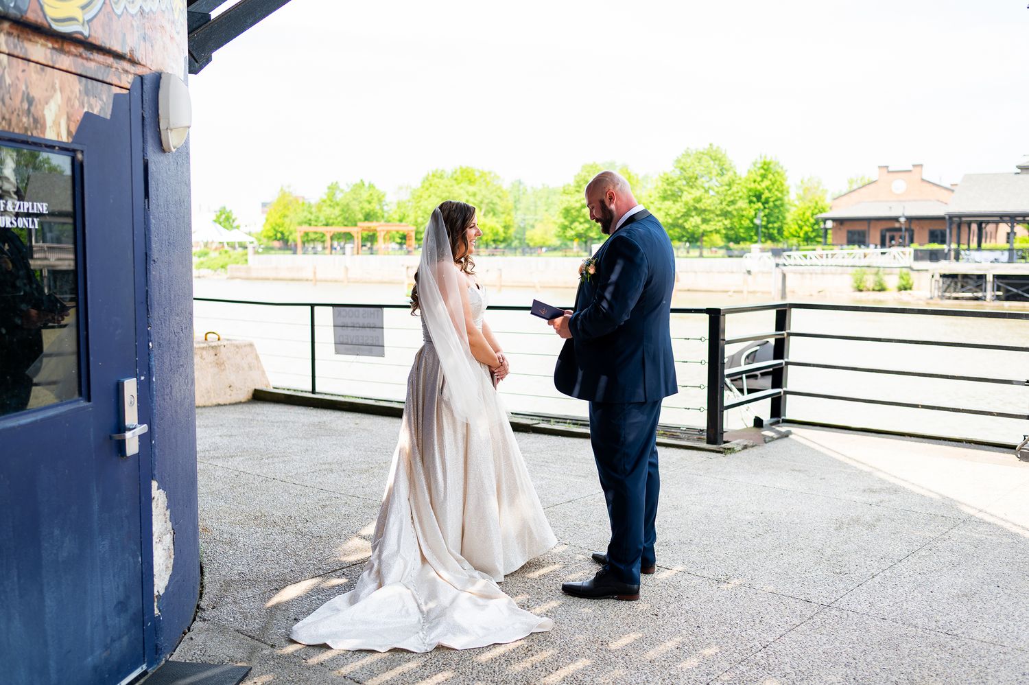 A couple shares an intimate moment during their first look on a covered deck overlooking a waterfront venue.