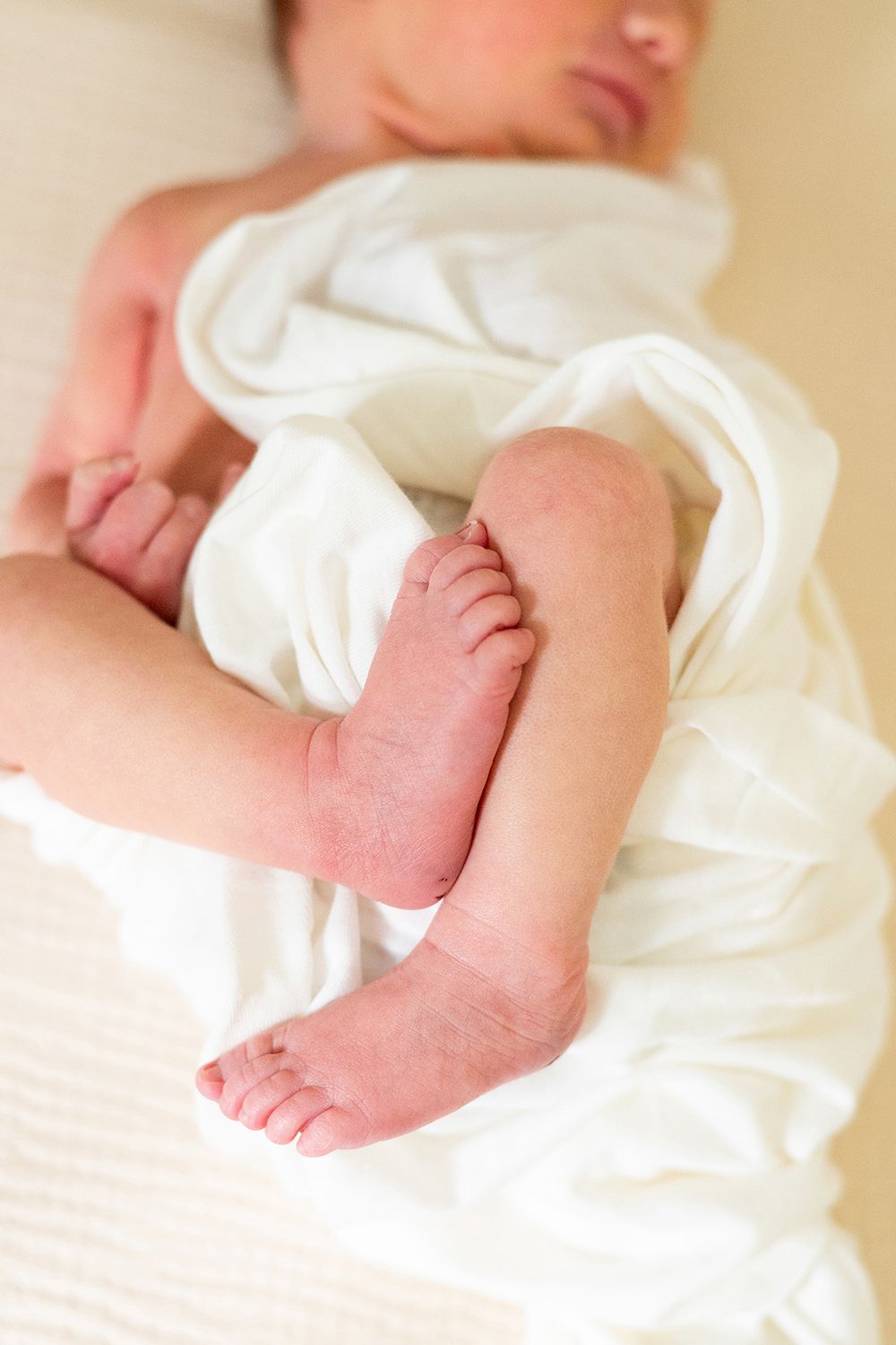 Close up of baby's tiny feet and legs wrapped in soft white blanket.