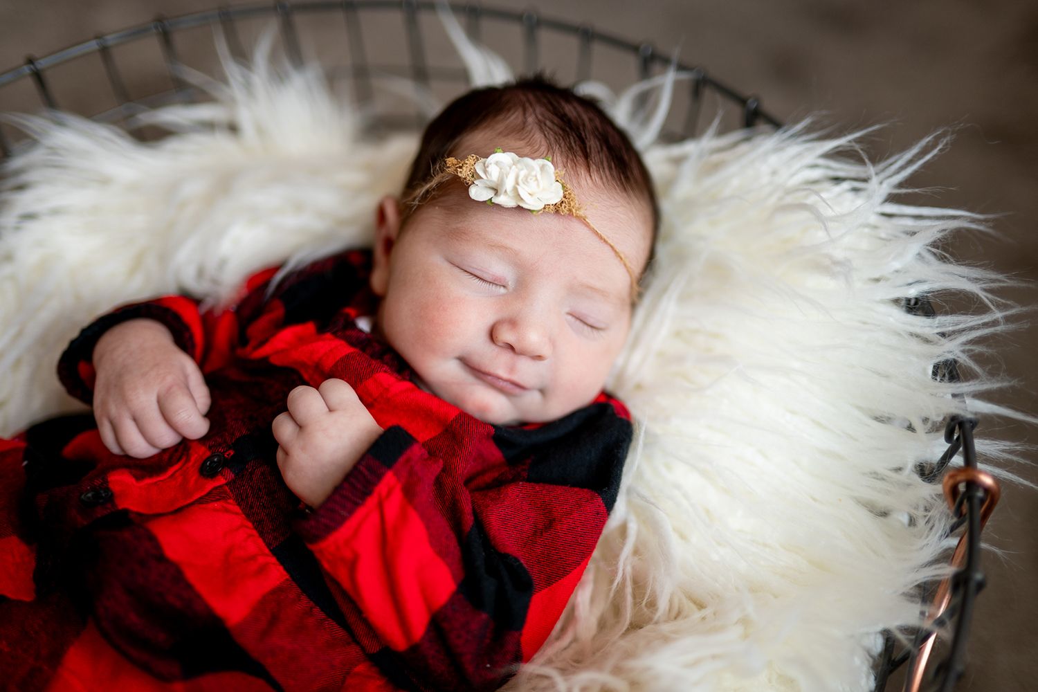 Sleeping baby in buffalo plaid outfit nestled on fluffy white fur backdrop.