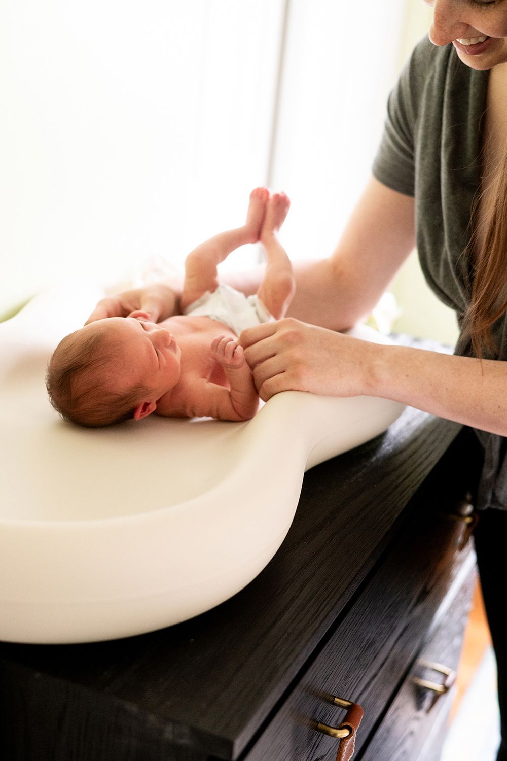 Caregiver changing or examining newborn baby on white changing pad.
