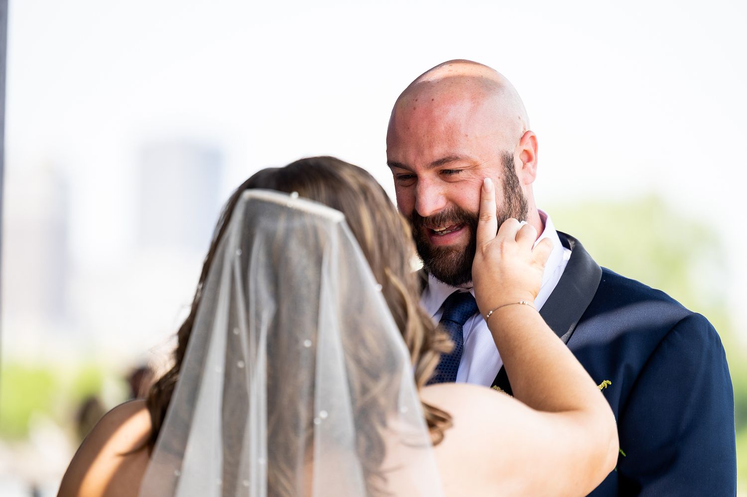 A couple shares an emotional moment during their wedding ceremony as the bride wipes away tears under her veil.