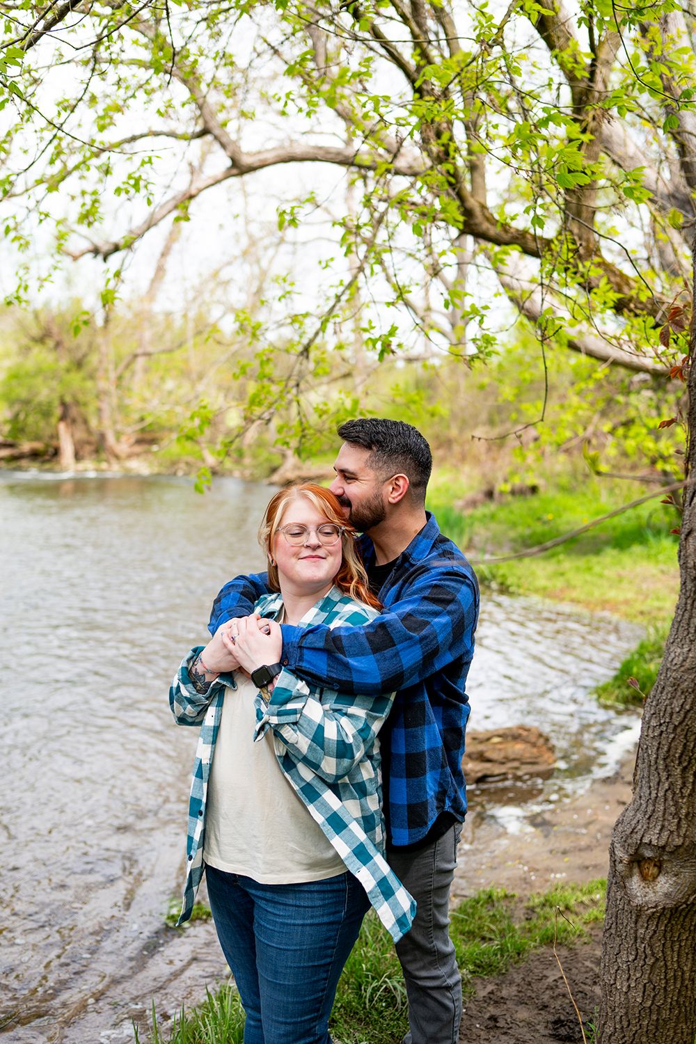 Casual engagement photos in a natural setting by a lake with greenery and trees in spring.