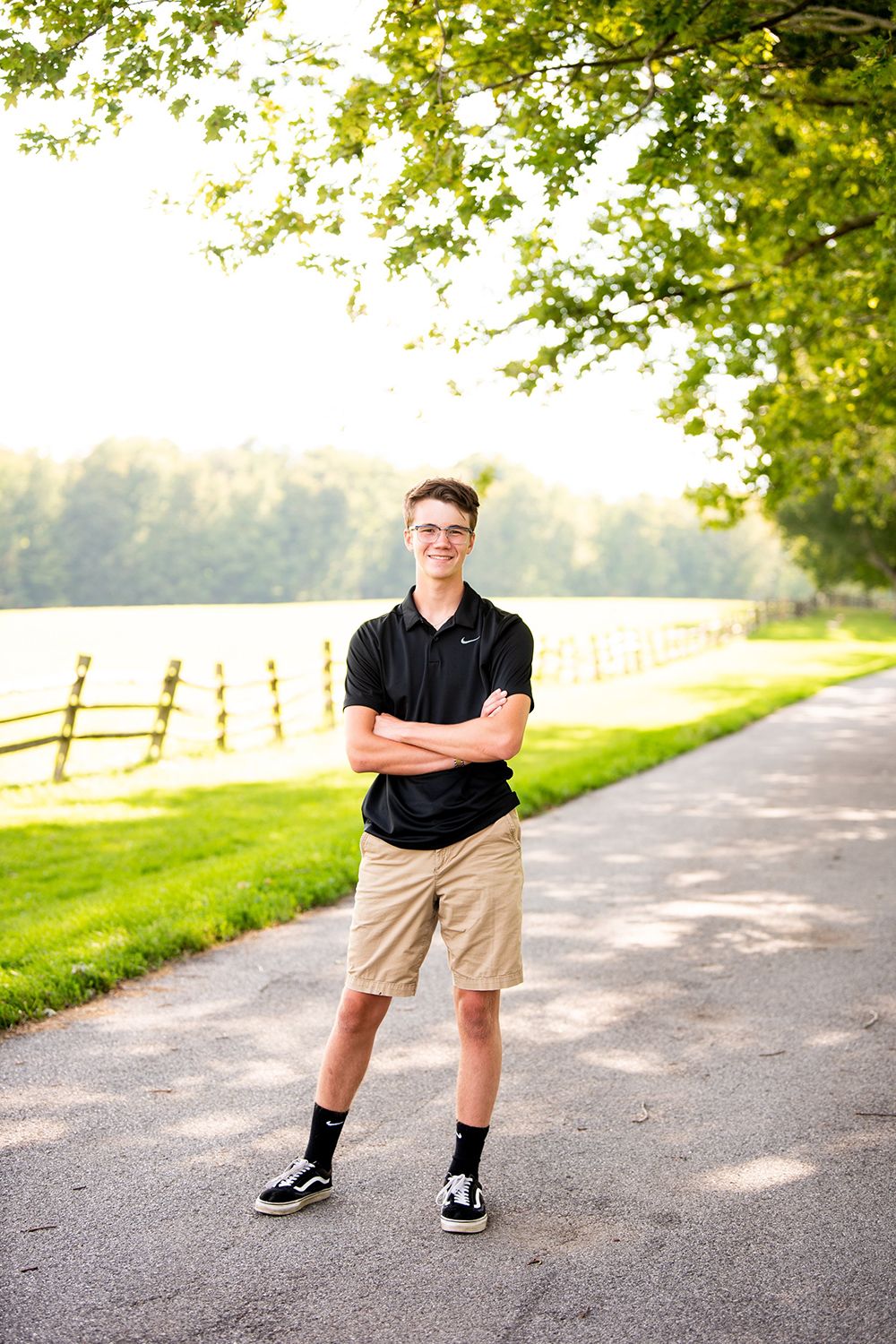 An outdoor portrait on a tree-lined path with rolling fields and a wooden fence in the background.