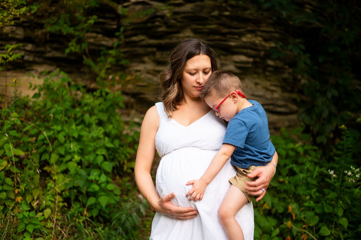 A tender maternity photo session in a lush garden with white dress and natural greenery backdrop.