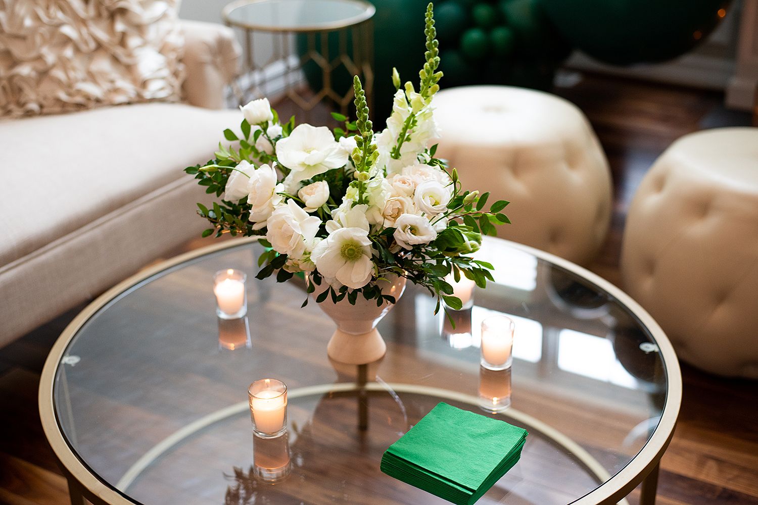 Elegant floral centerpiece with white flowers and greenery sits atop a round silver table with glowing candlelight.