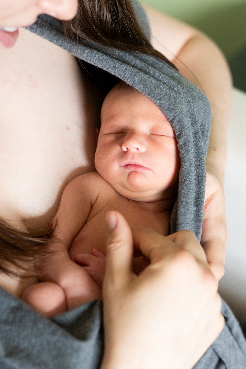 A sleeping newborn wrapped in a soft grey blanket is being gently held close.