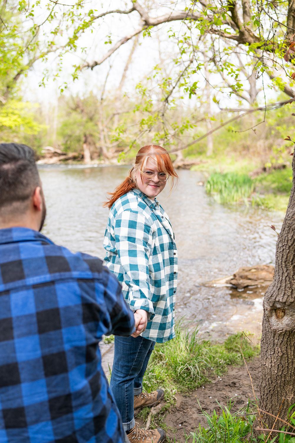 Two people in plaid flannel shirts spend time together by a scenic river on a spring day.