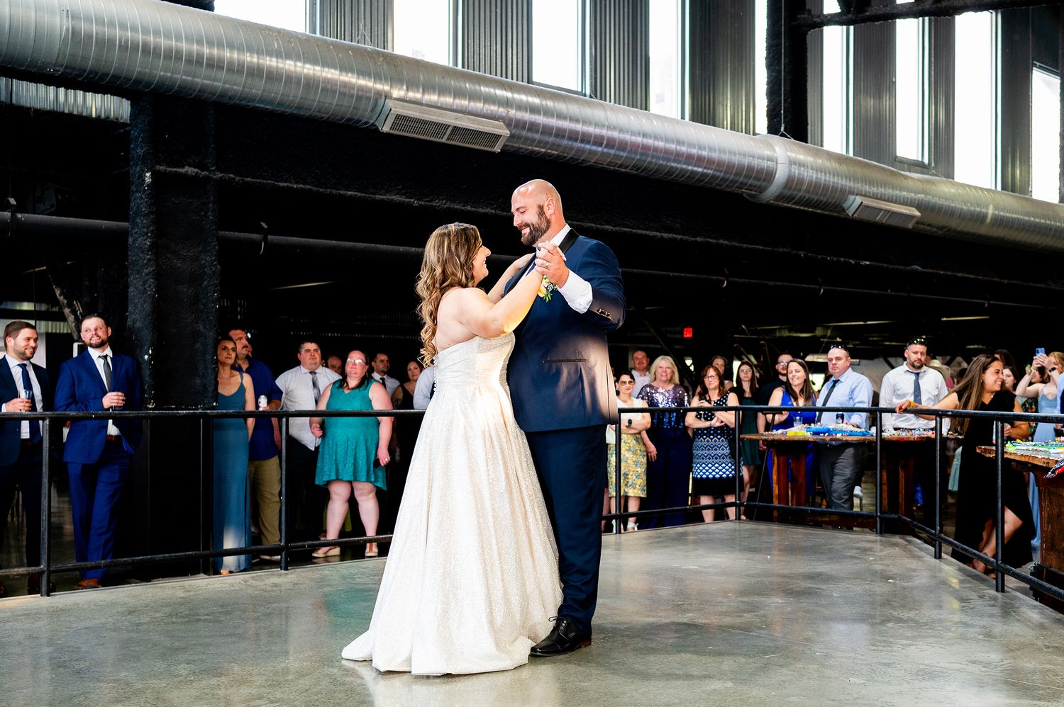 Wedding party dancing and celebrating in a spacious indoor venue with large windows.