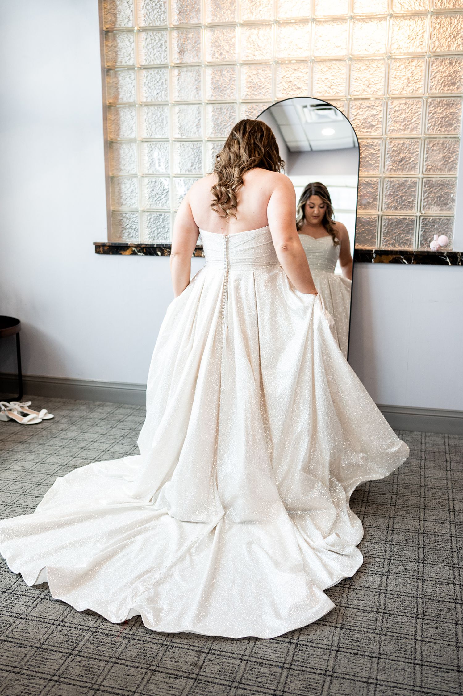 Two people in elegant white wedding dresses sit together on a carpeted floor showing the flowing fabric and trains.
