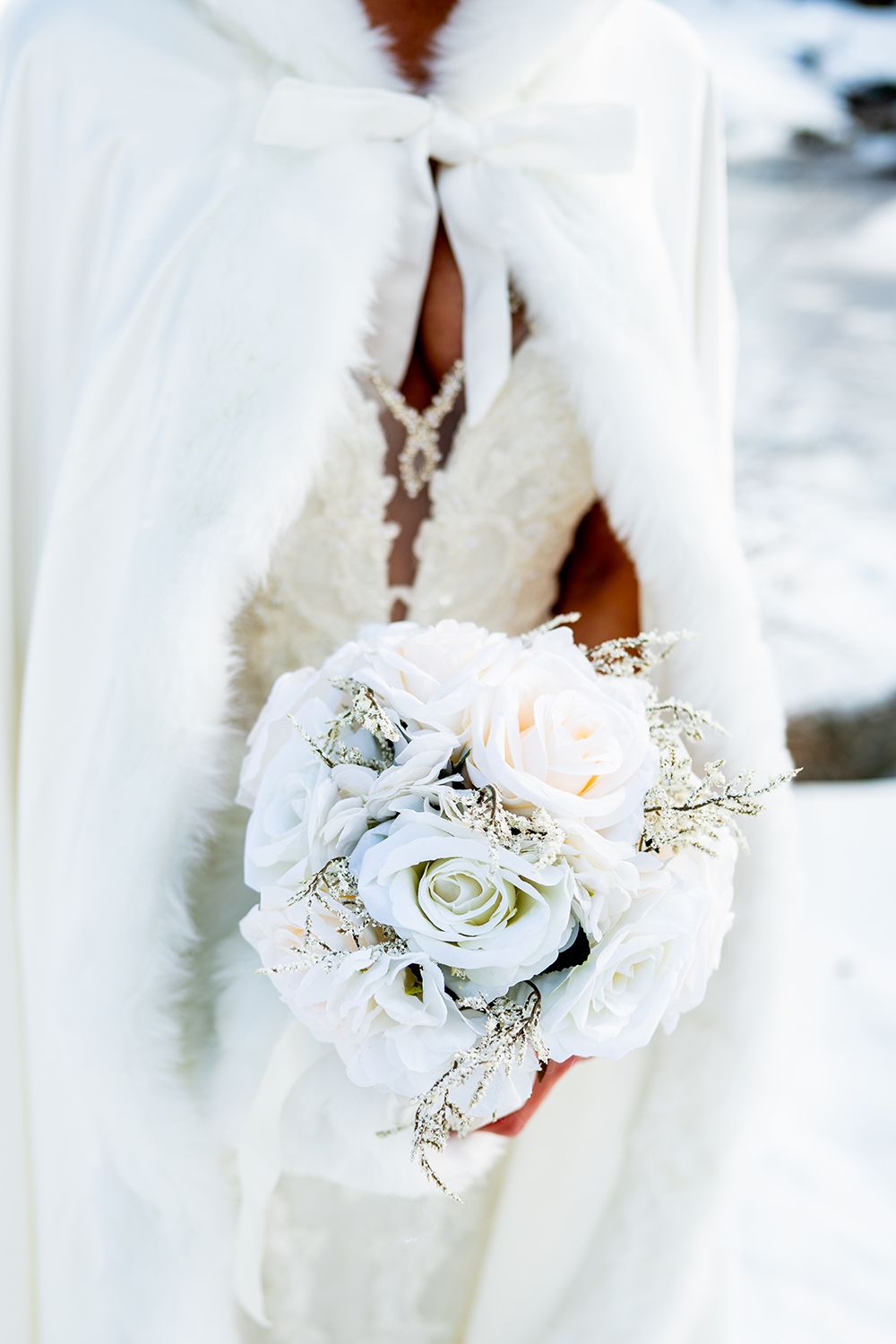 A delicate bridal bouquet with white and blush roses with baby's breath against a flowing white dress.