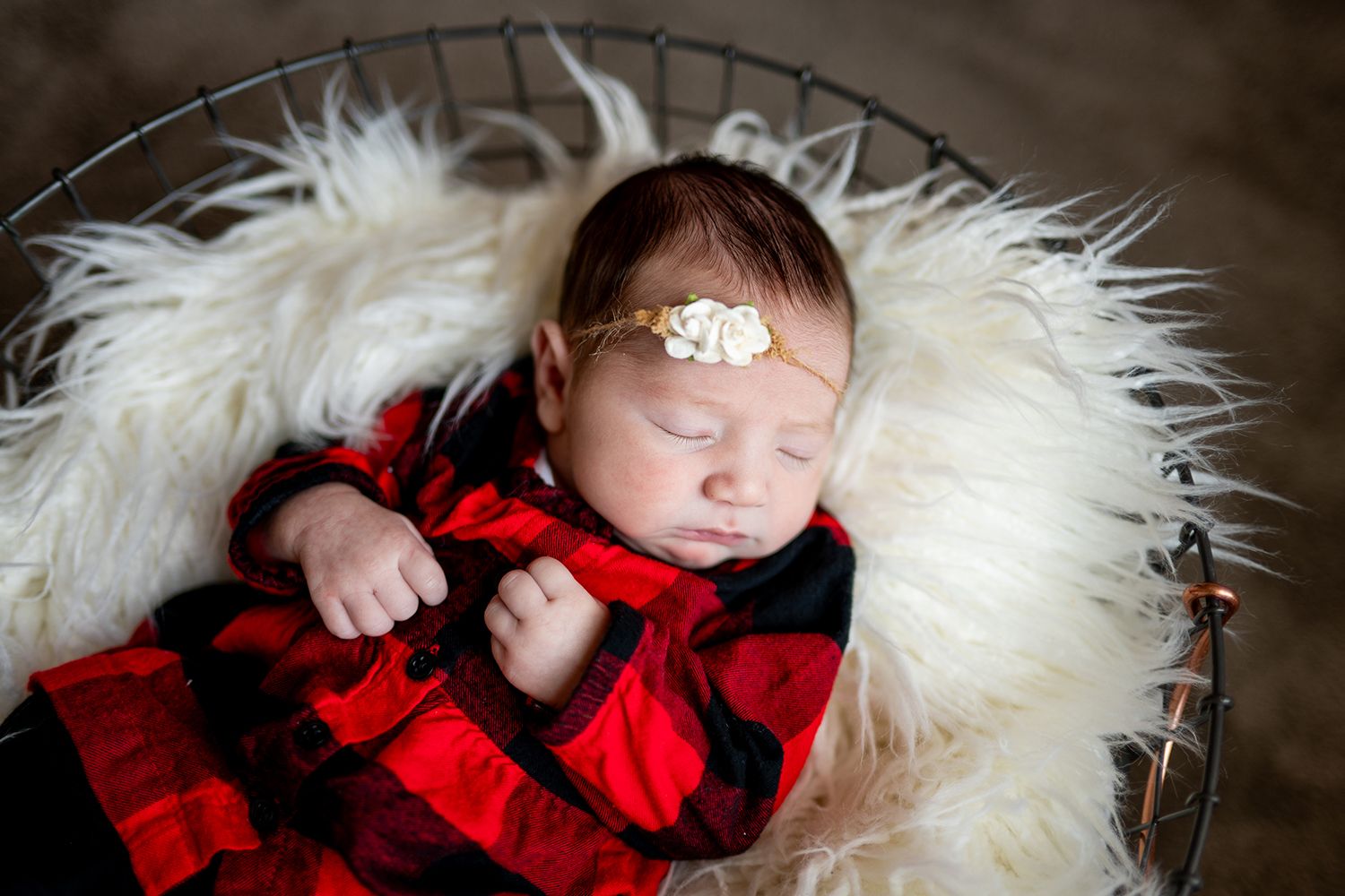 Baby wearing red and black plaid outfit asleep on soft white fur blanket.