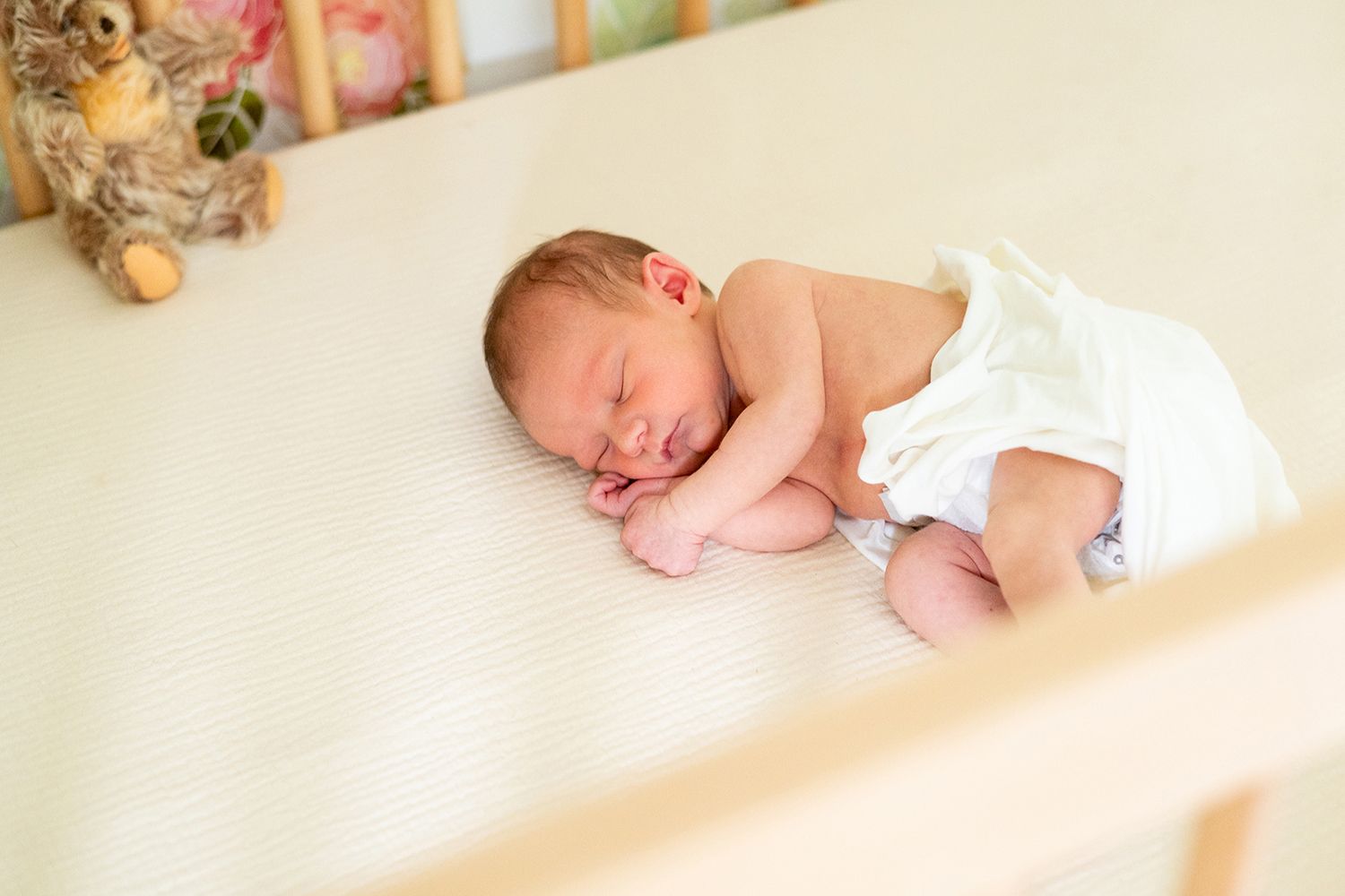 Peaceful newborn baby sleeping in white crib with stuffed animal nearby.